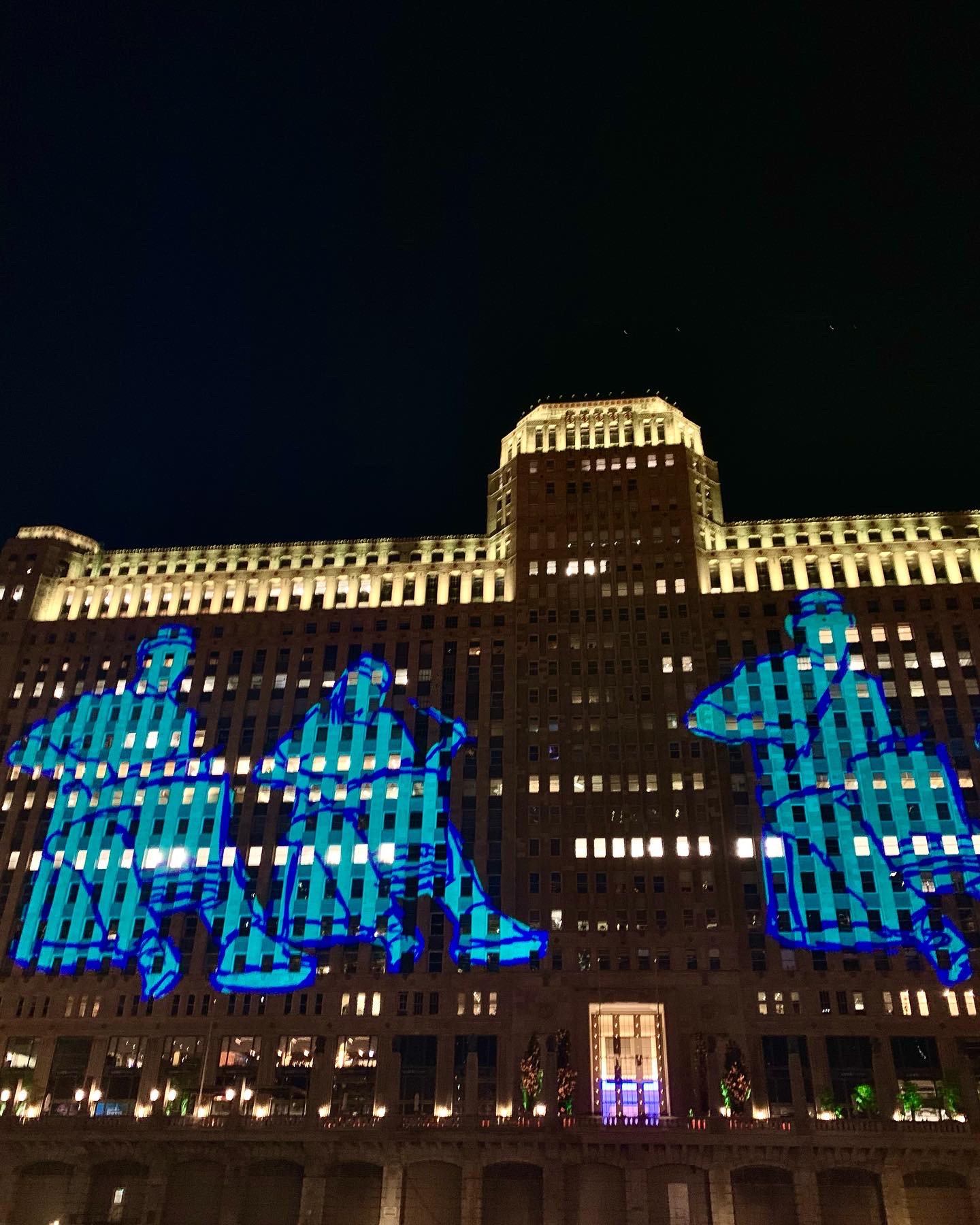 Giant blue figures projected across the Merchandise Mart facade at night