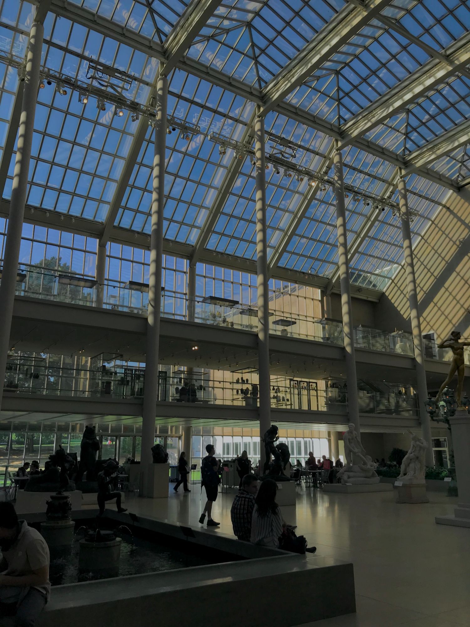 A glass-roofed museum sculpture court, evening light through the panes