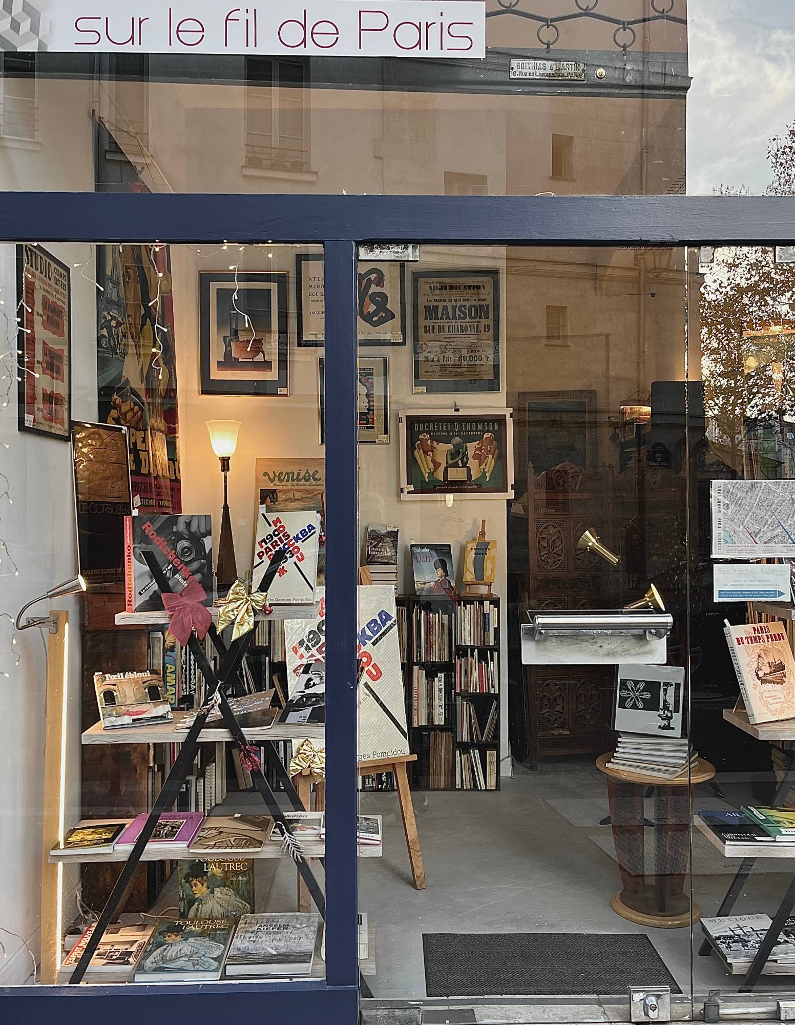 A vintage poster and book shop window in Paris, warm light inside