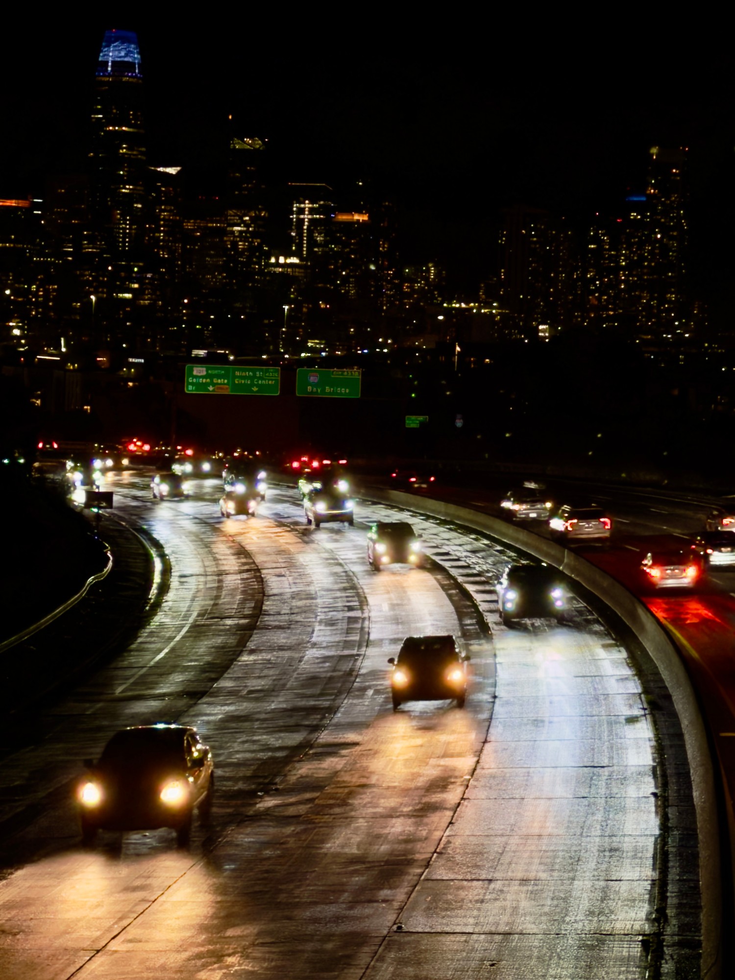 Wet freeway lanes curving toward the San Francisco skyline at night